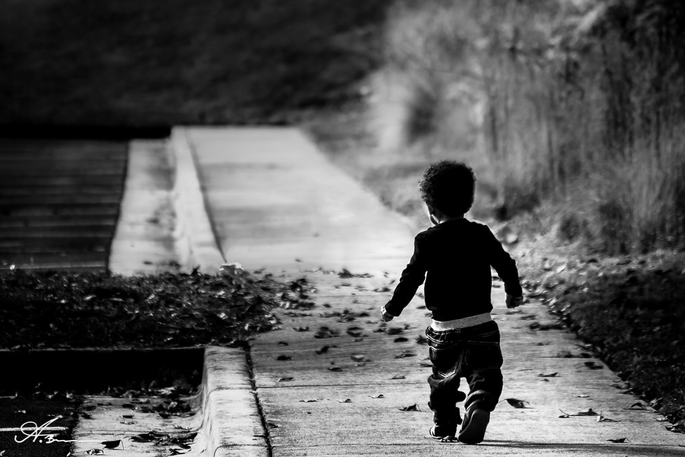 Black and white image of an African American boy walking on pavement